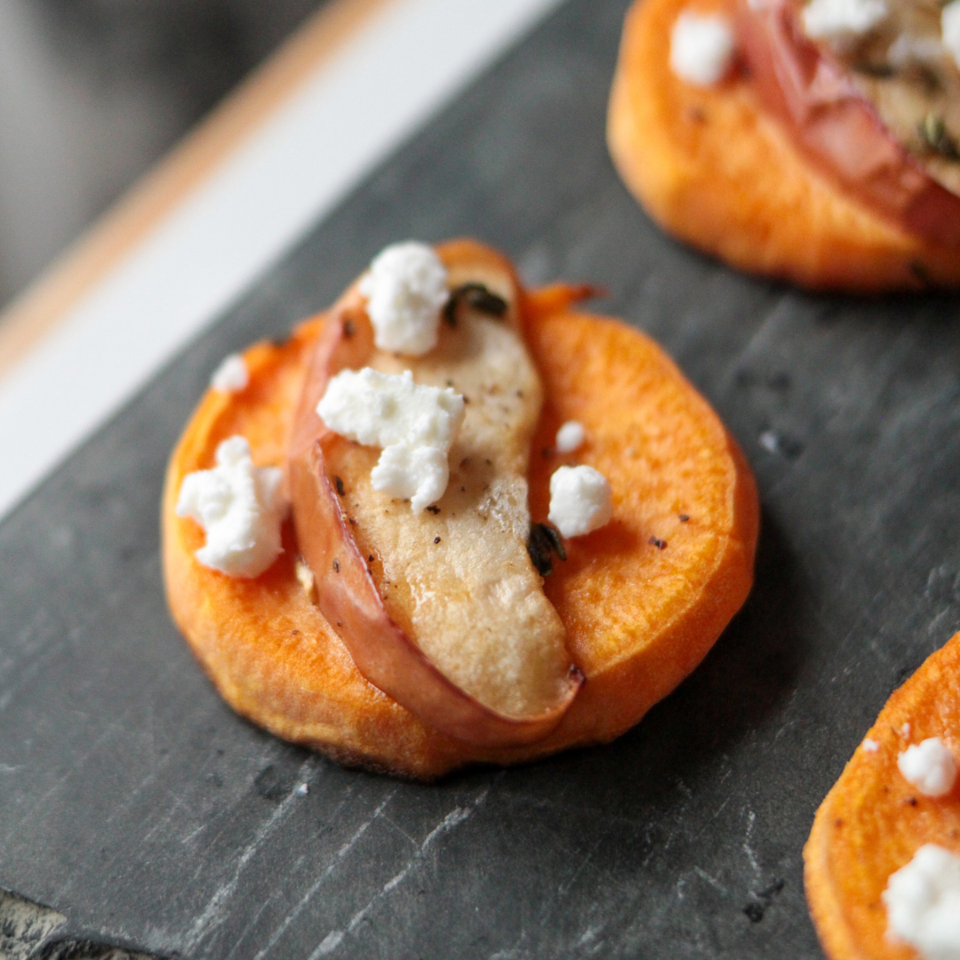 5 Sweet potato round topped with apple slice and goat cheese. Sitting on a black stone board.
