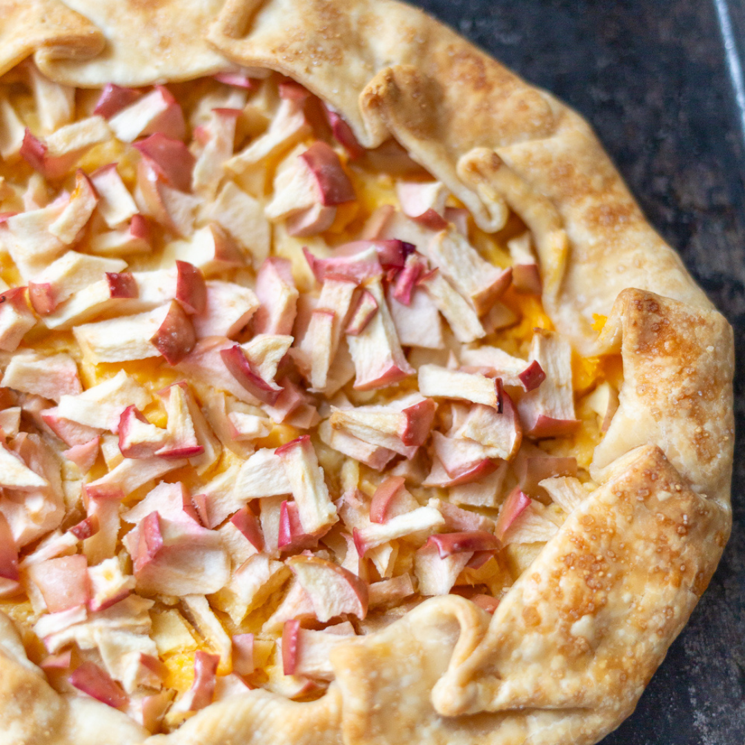 6 Open faced pastry with open face containing diced apples covering custard. Galette is sitting on a black stone board.